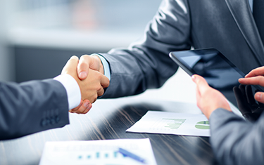 Dos personas dándose la mano mientras otra consulta algo en la tablet